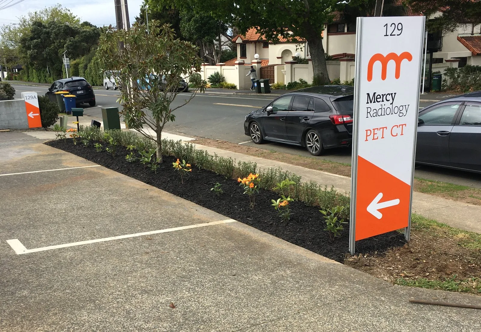 A newly planted and mulched bed running the length of a medical centre car park, beside its entrance sign