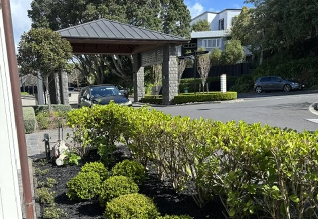 Ball topiary and a trimmed hedge in black mulch, framing the entrance pavilion of a retirement village