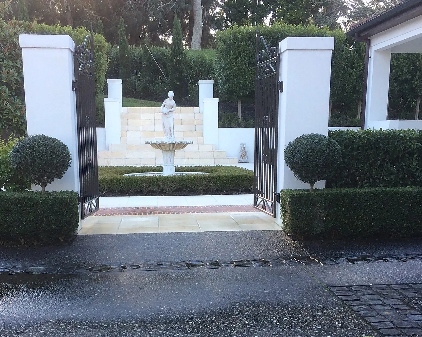 A gated entrance with clipped hedging, ball topiary and a fountain beyond