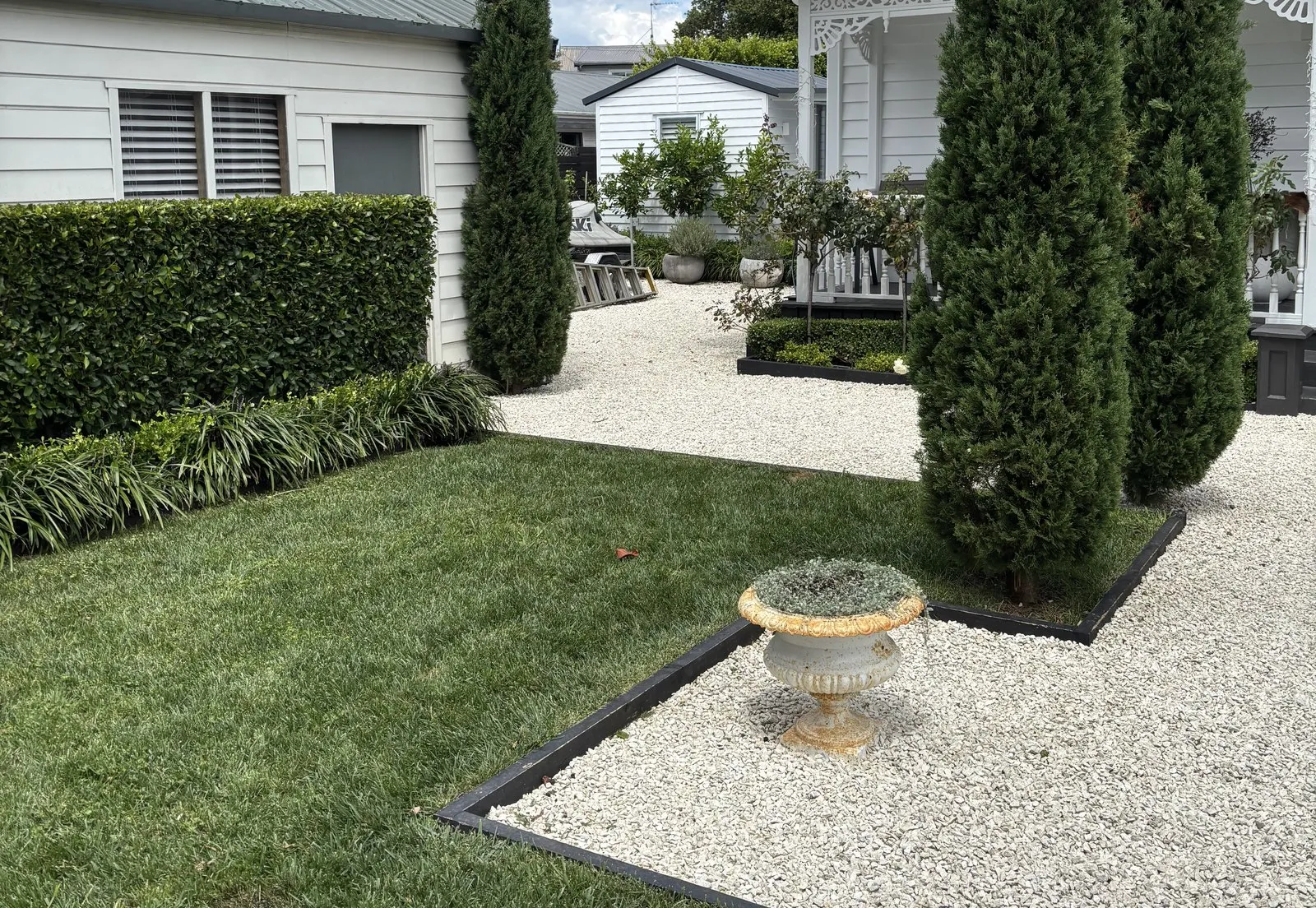 Clipped conical topiary and a stone urn on raked gravel, against a crisp lawn edge